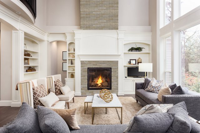 Beautiful living room interior with tall vaulted ceiling, loft area, hardwood floors and fireplace in new luxury home. Has large bank of windows